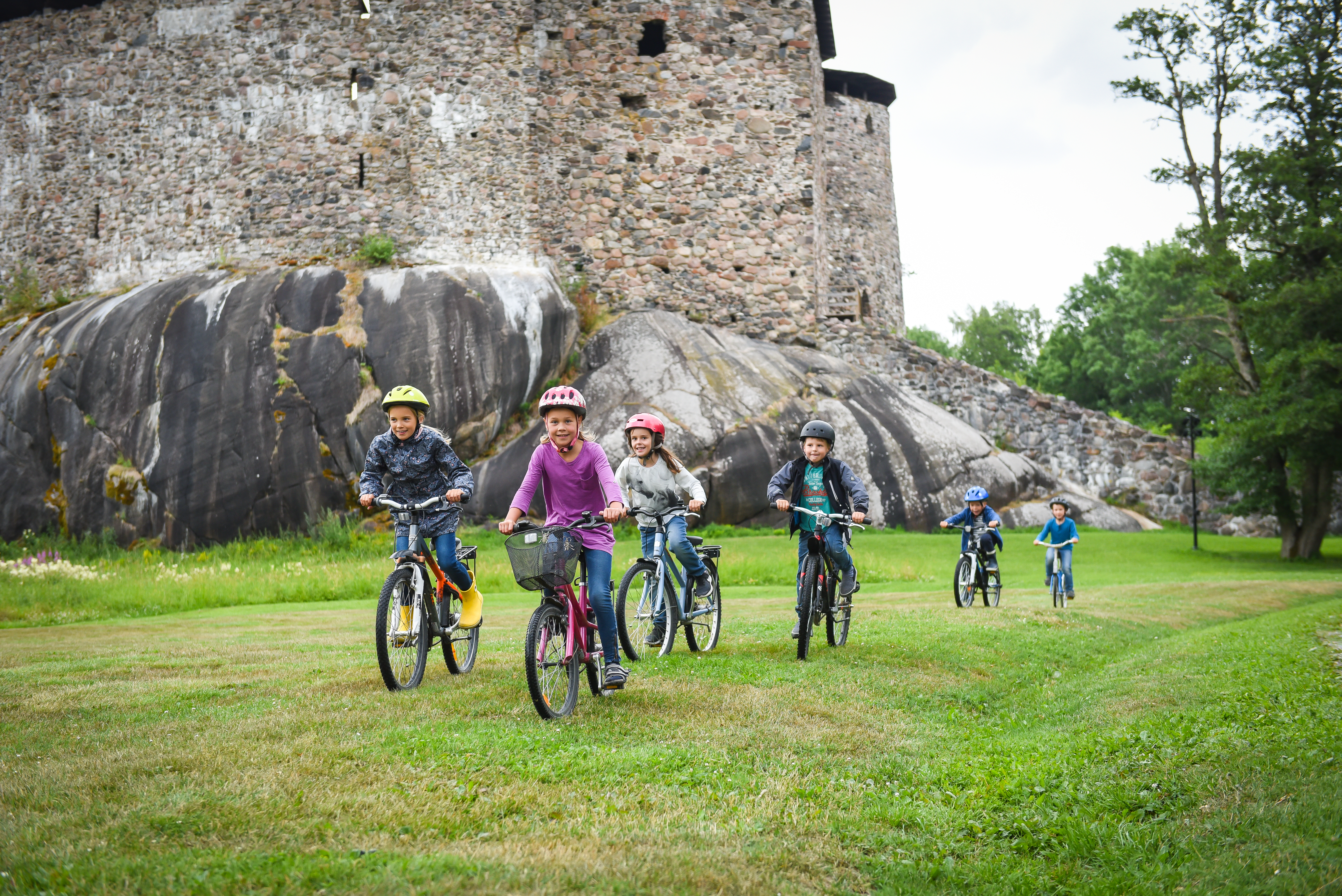 Ryhmä lapsia pyöräilevät Raaseporin linnanraunoiden edessä